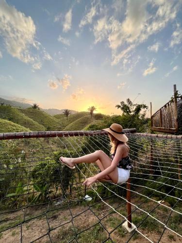 a woman in a hat sitting on a fence at The Valley Tayrona hostel- A social jungle hostel in El Zaino