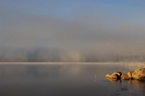 a misty lake with rocks in the middle of the water at Hotell Tjamstan Malå in Malå
