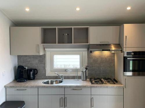 a kitchen with white cabinets and a sink and a window at Chalet (J09) op gezellige familiecamping bij zee in Kamperland