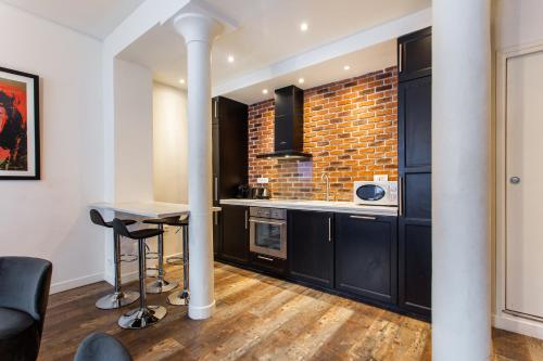 une cuisine avec des armoires noires et un mur en briques dans l'établissement MBM - Paradis, à Paris