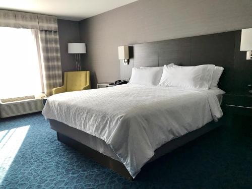 Holiday Inn Express Sidney, an IHG Hotel في Sidney: غرفة نوم بسرير كبير عليها شراشف ووسائد بيضاء