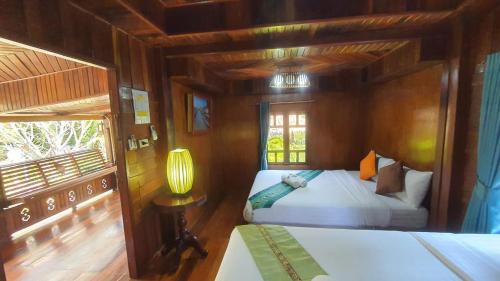 a bedroom with two beds and a lamp and a window at บ้านสวนในฝัน-ตลาดน้ำท่าคา in Samut Songkhram