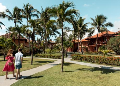 a man and woman walking down a sidewalk in front of palm trees at Pousada Tabapitanga in Porto De Galinhas