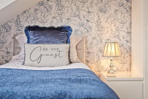 a bedroom with a blue bed with a be our guest pillow at Broadlands Windermere in Windermere