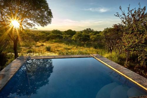 a swimming pool in the middle of a field with the sun setting at ZuriCamp - Tent Madini in Tsumeb