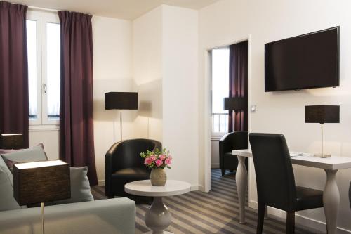 ein Hotelzimmer mit einem Wohnbereich mit einem Tisch und Stühlen in der Unterkunft Executive Hôtel Paris Gennevilliers in Gennevilliers