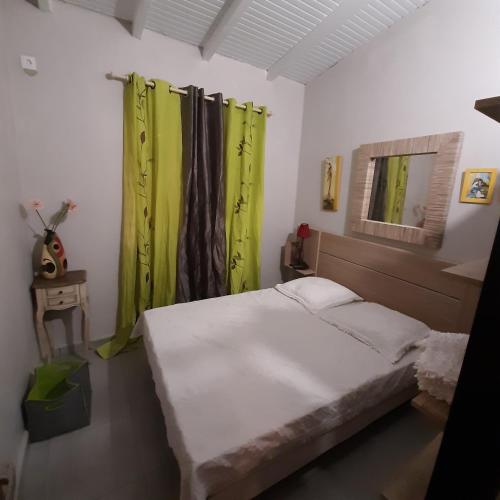 a small bedroom with a bed and green curtains at Charmant bungalow du Moule in Le Moule