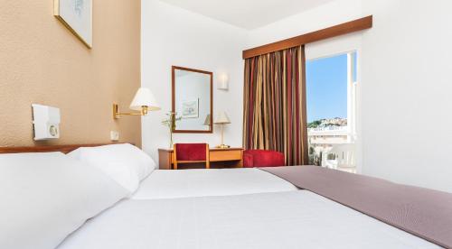 a hotel room with a bed and a desk and a window at Globales Playa Santa Ponsa in Santa Ponsa