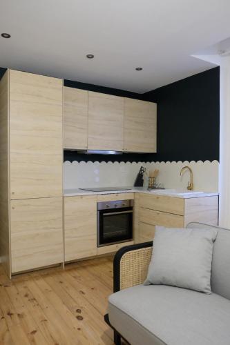 a kitchen with wooden cabinets and a couch in a room at HIMA, Beau T2 rénové à neuf Châteaucreux Gare in Saint-Étienne