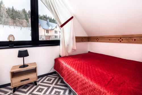 a bedroom with a red bed and a window at FAJNE CHATY - rodzinny wypoczynek w górach in Falsztyn