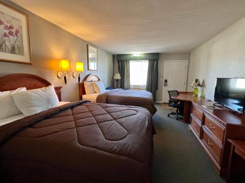 a hotel room with two beds and a desk and a television at Ozark Inn & Suites in Ozark