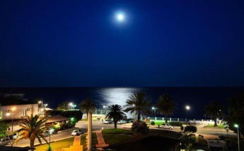 a full moon over a city with palm trees and the ocean at Hotel Mediterraneo in Roccella Ionica