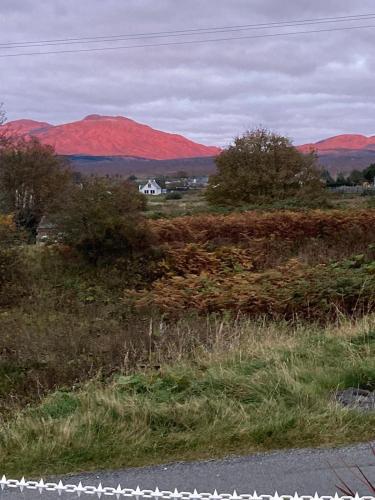 a white house in a field with mountains in the background at Skerrols in Broadford