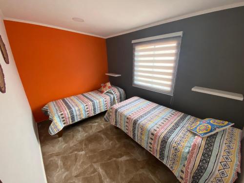 two beds in a room with orange walls and a window at Casa Campanario - San Pedro de Atacama, Desconéctate! in San Pedro de Atacama