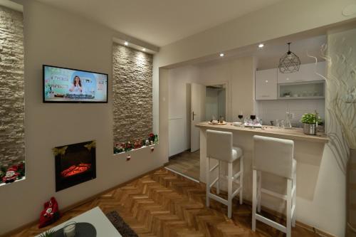 a kitchen with a bar with white chairs and a fireplace at Gold apartman Vršac in Vršac