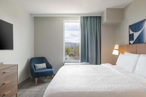 a bedroom with a bed and a blue chair and a window at Staybridge Suites Rochester - Mayo Clinic Area by IHG in Rochester