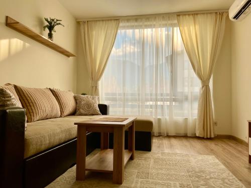 een woonkamer met een bank en een tafel voor een raam bij Pirin Dream View Apartments in Razlog