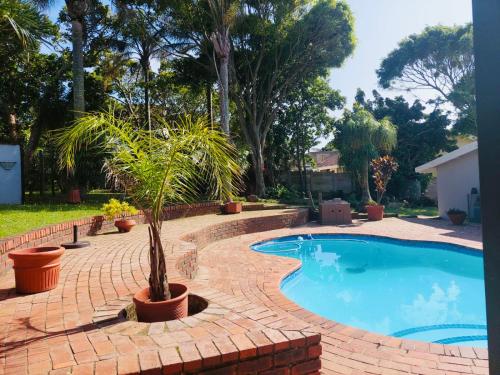 a swimming pool with a palm tree next to a brick walkway at Beautiful Villa - Scottburgh, Durban in Scottburgh