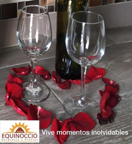 two wine glasses sitting on a table with red flowers at Posada Equinoccio in Bernal