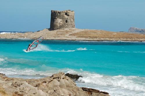 a person windsurfing in the ocean near a lighthouse at Hotel Geranio Rosso in Stintino