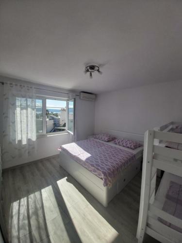 a white bedroom with a bed and a window at Apartman Maslov in Duće