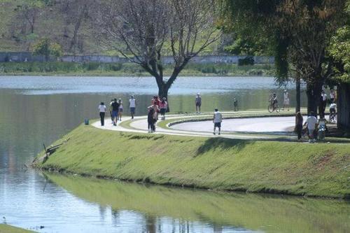 a group of people walking around a park next to a lake at Flat com Varanda-Pampulha in Belo Horizonte