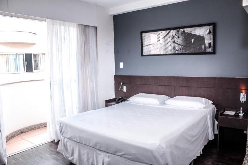a bedroom with a large white bed and a window at Flat com Varanda-Pampulha in Belo Horizonte