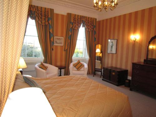 a bedroom with a bed and two chairs and two windows at Georgian Guest House in Edinburgh