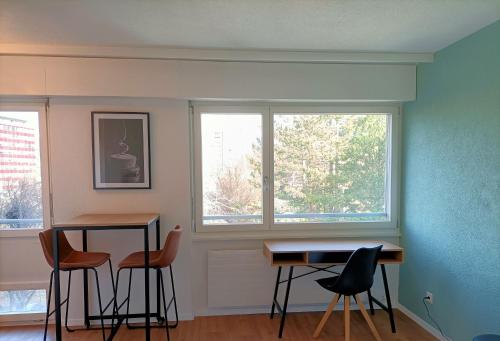 une chambre avec une table, des chaises et deux fenêtres dans l'établissement Studio lumineux bien placé en ville de Sion, à Sion