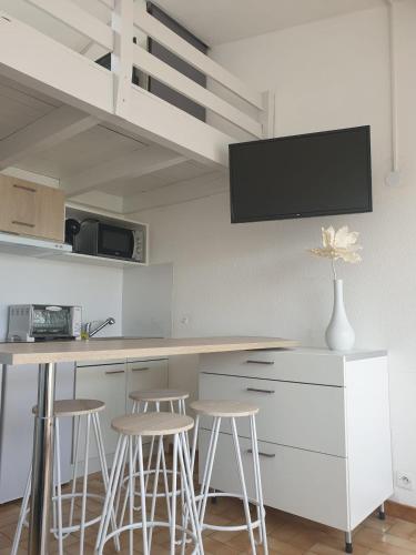 d'une cuisine avec des tabourets et un comptoir avec une télévision murale. dans l'établissement Studio meublé cap d Agde avec tres belle vue sur le port, au Cap d'Agde