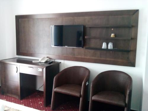 Habitación de hotel con 2 sillas, escritorio y TV. en Pensiunea Clasic, en Curtea de Argeş