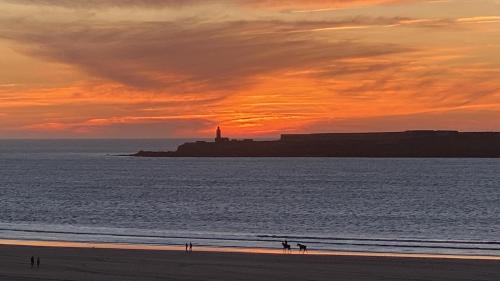 a sunset at the beach with a lighthouse in the distance at PRESTIGIA ESSAOUIRA MOGADOR Luxury Ocean View in Essaouira