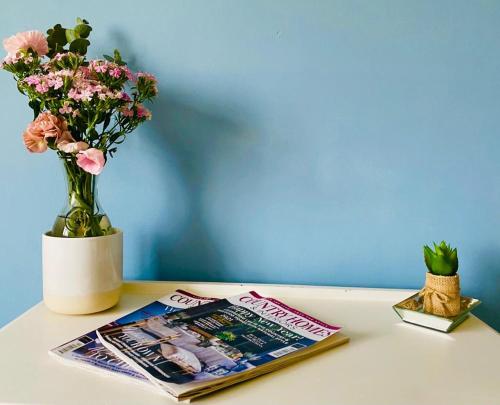 a table with a magazine and a vase with flowers at Fern Cottage Iden, Rye in Iden