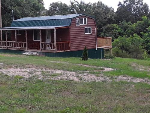 a red house with a porch on a field at Amish made cedar cabin with a loft on a buffalo farm close to the Buffalo River in Marshall