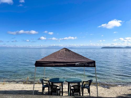 two tables and chairs under an umbrella on the beach at Biwa-Lakeside Cottage B B Dylan in Minami-komatsu