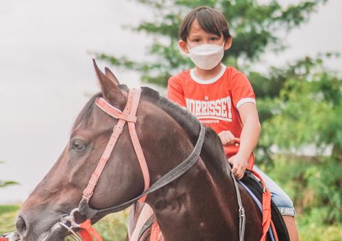 a young child wearing a mask riding a horse at Shanaya Resort Malang in Malang