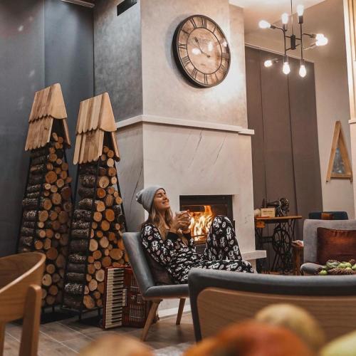 a woman sitting in a chair in front of a fireplace with a clock at Casa di Pino EcoLodge Hotel in Žabljak