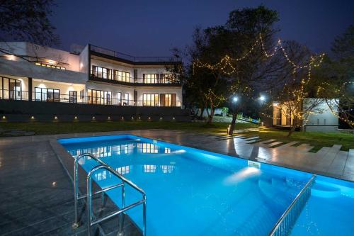 a swimming pool in front of a house at night at Earth Song by StayVista - Boasting an Open theatre, Games, Spacious lawn, Swimming pool & Conference room in Pune