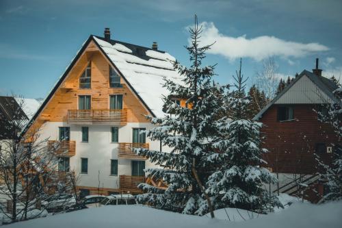 a house with a snow covered tree in front of it at Casa di Pino EcoLodge Hotel in Žabljak