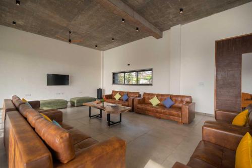a living room with leather couches and a table at Earth Song by StayVista - Boasting an Open theatre, Games, Spacious lawn, Swimming pool & Conference room in Pune