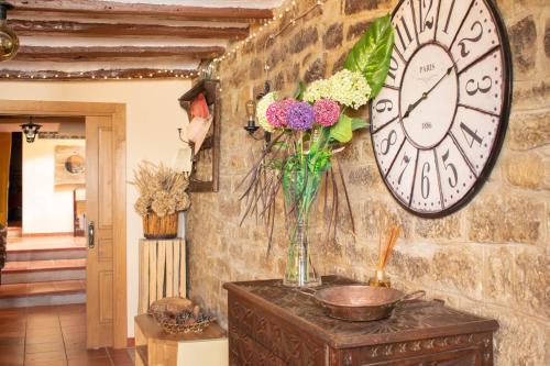 un reloj en una pared con un jarrón de flores en una mesa en Casa rural Ezkonberri, en Unzué