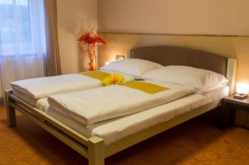 Una cama con dos almohadas blancas y una flor. en Hotel Lužnice, en Planá nad Lužnicí