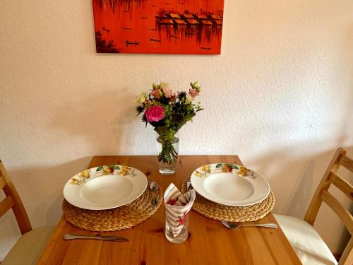 a wooden table with two plates and a vase of flowers at UPGRADE - frisch renoviert - Ferienwohnung Monteuerswohnung am Bauernhofweg in Lohmar nahe S-Bahnhof Messe Flughafen in Lohmar