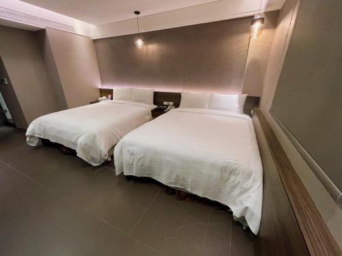 two beds in a hotel room with white sheets at OUGE Motel - Fengshan in Kaohsiung