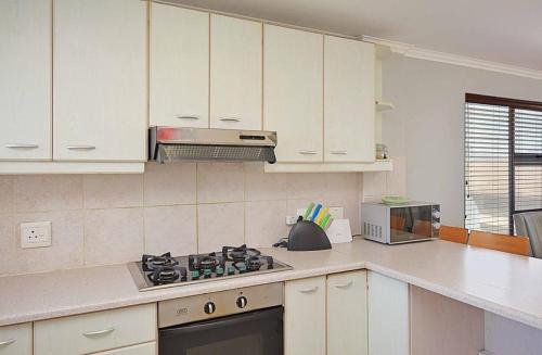 a kitchen with white cabinets and a stove top oven at Nautica 2 Bedroom Beachfront Apartment with Sea Views in Bloubergstrand