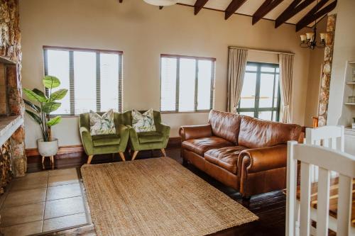 a living room with a leather couch and two chairs at Blue Crane Farm Lodge in Botrivier