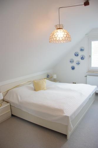 a white bed in a white room with a chandelier at Haus Burmeister in Tinnum