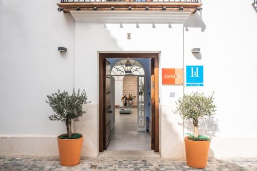 uma porta aberta para um edifício branco com dois vasos de plantas em Amphora Alojamiento Ecija em Écija