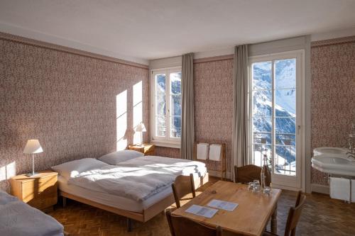 a bedroom with a bed and a table and windows at Hotel Regina in Mürren
