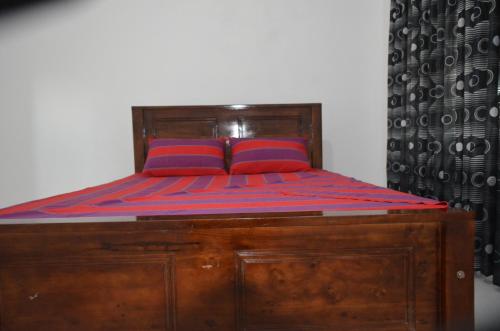 a wooden bed with two red pillows on it at Ruins Villa in Polonnaruwa